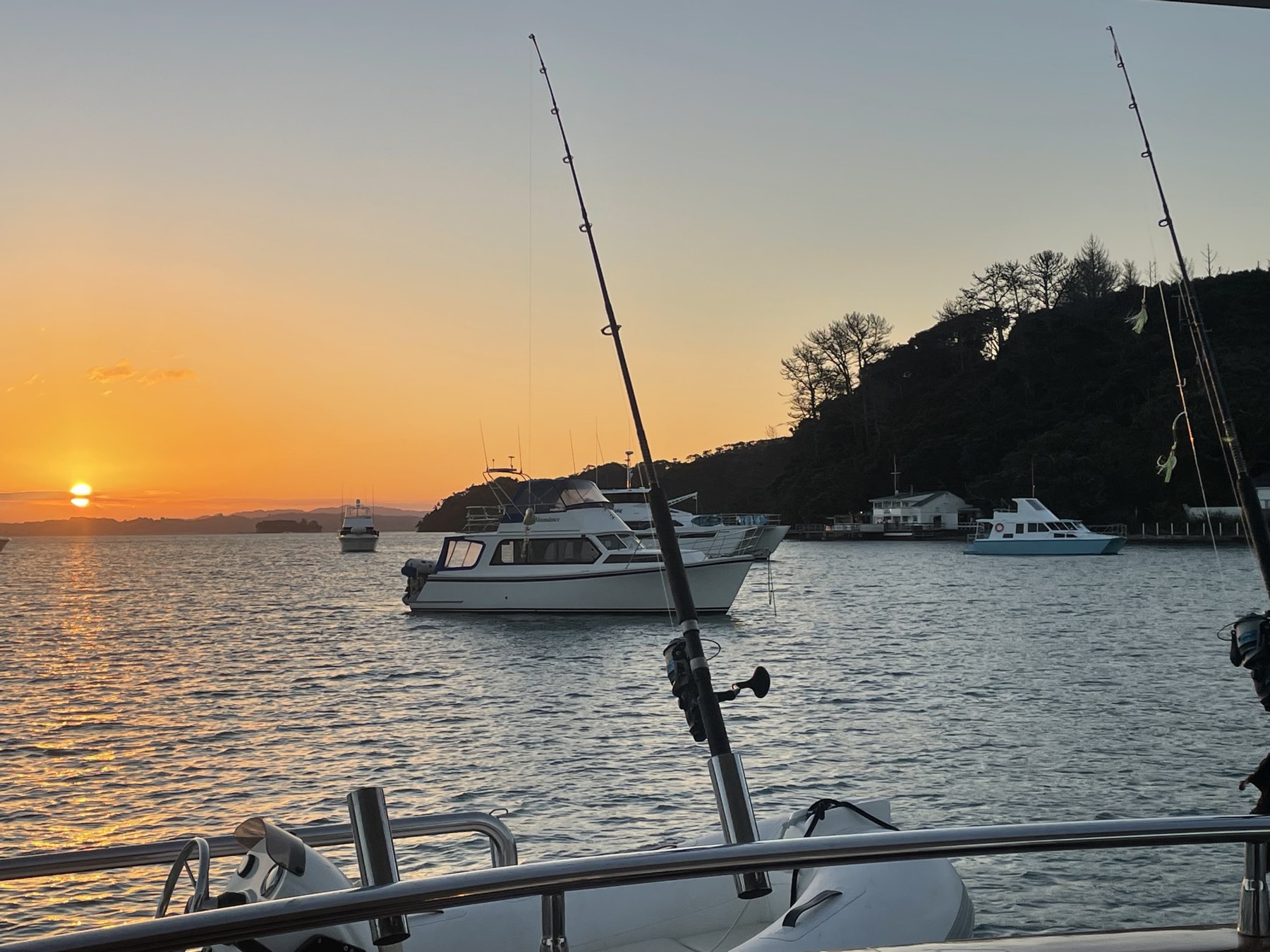 Sunset over a quiet anchorage on the Hauraki Gulf with fishing rods in the foreground